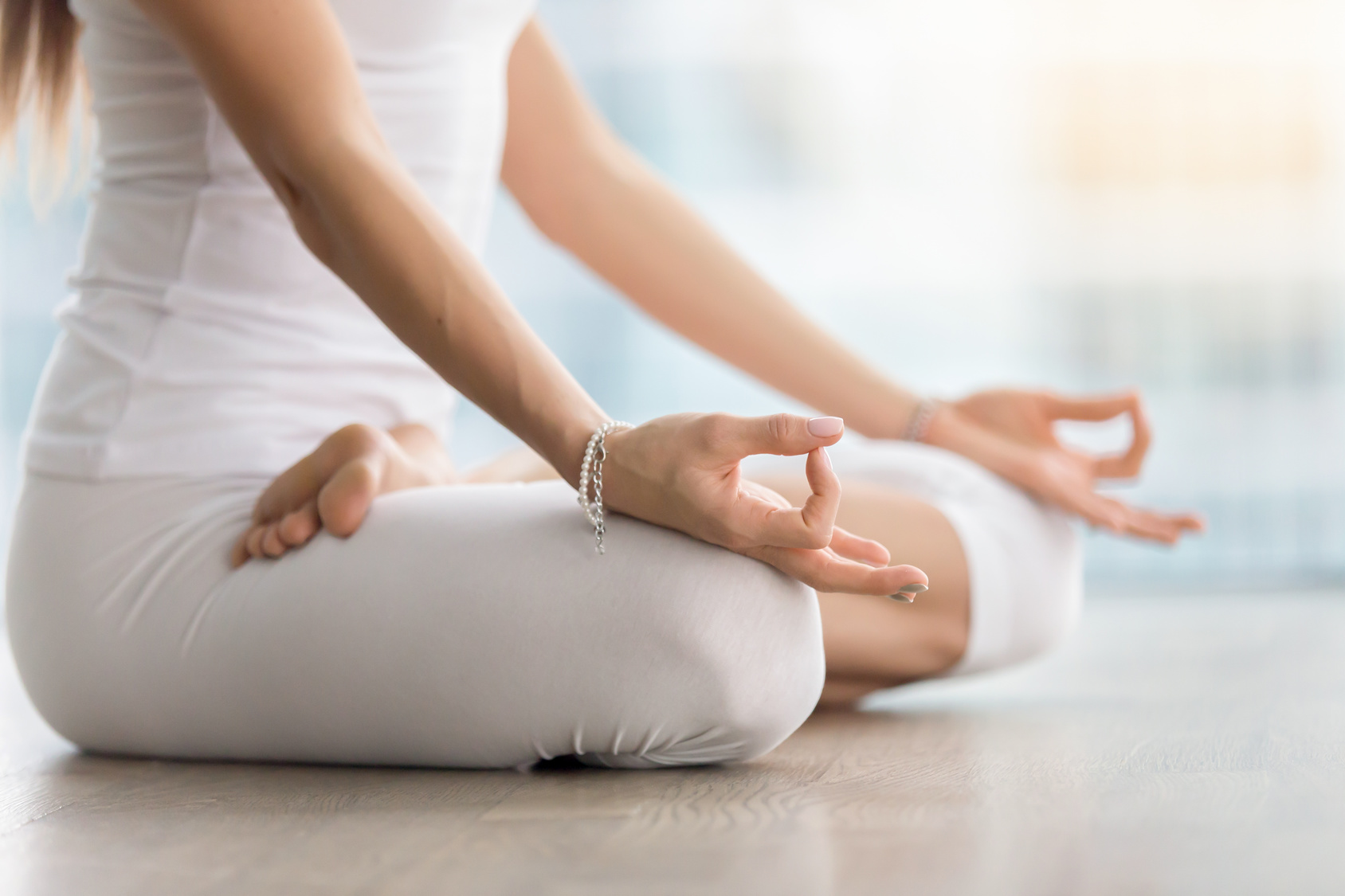Young attractive yogi woman practicing yoga, sitting in Padmasana, exercise, Lotus pose with mudra, working out, wearing white sportswear, indoor, meditation session near window. Midsection close up